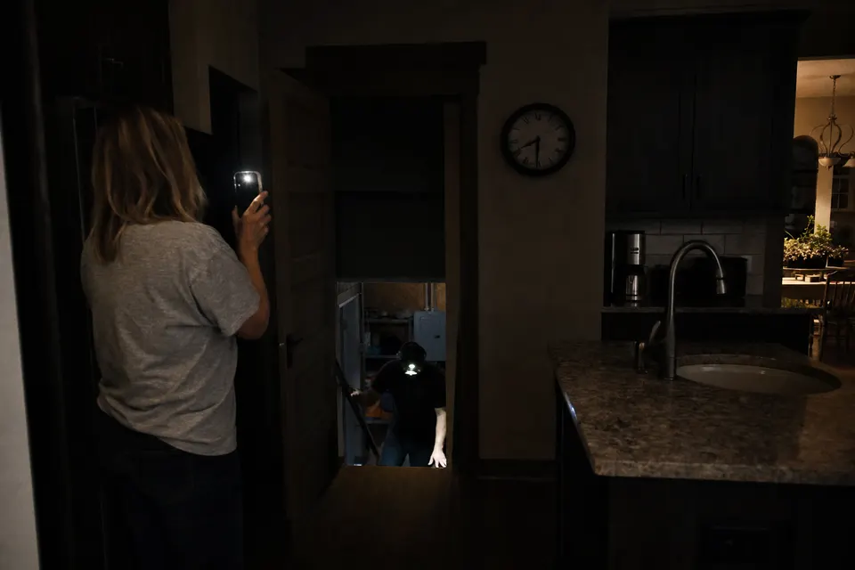 A Lockport kitchen half dark at night, a phone flashlight aimed at the basement door